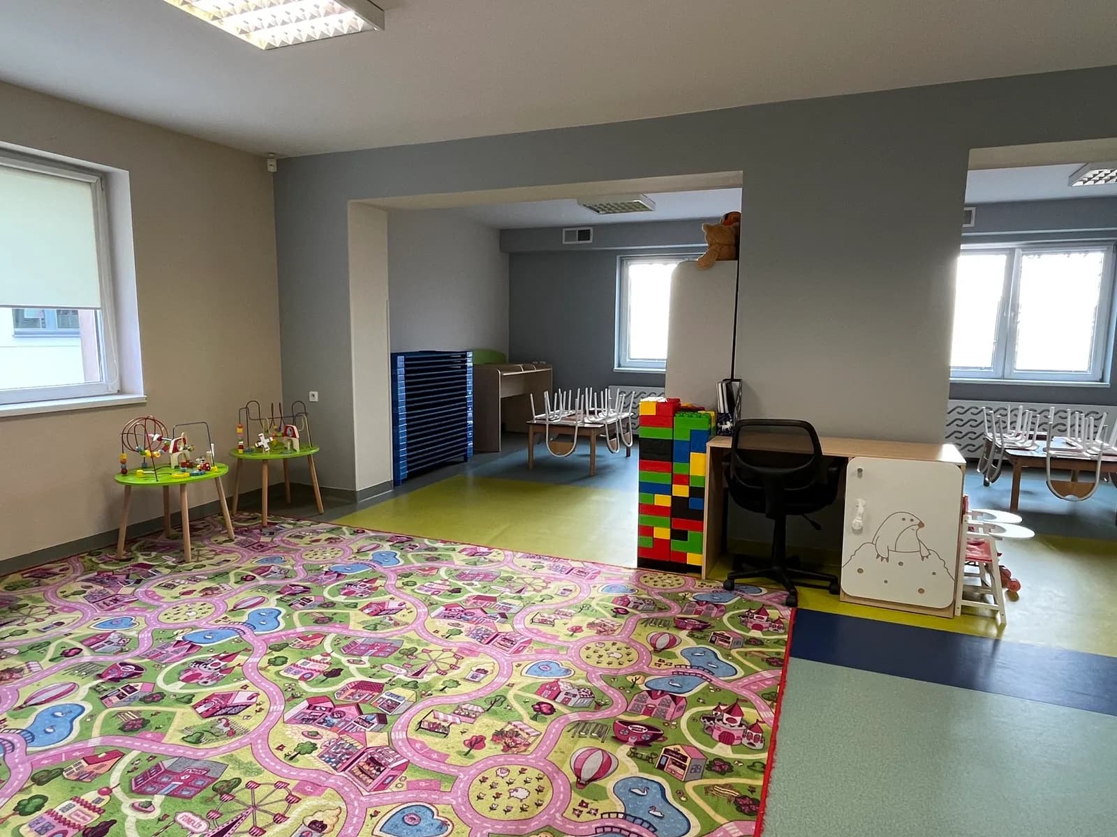 Kącik zabaw w sali przedszkolnej z dywanem i regałami na zabawki